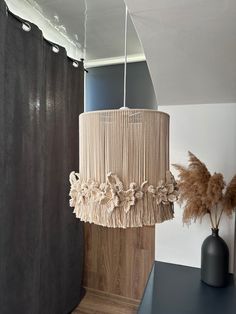 a lamp hanging from the ceiling next to a vase with dry grass in it on a table