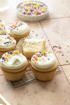 cupcakes with white frosting and sprinkles on a cooling rack