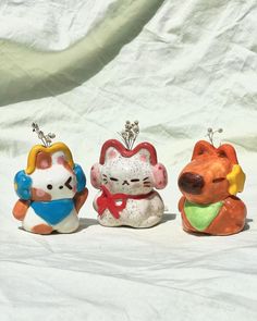 three small ceramic figurines are sitting on a white sheet