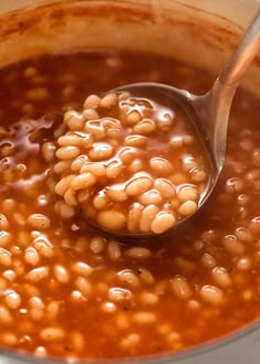 a ladle full of beans is being stirred by a spoon in a saucepan