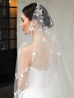 a woman wearing a wedding veil with white flowers on the back of her head and shoulder