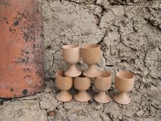 a group of wooden cups sitting on top of a dirt ground next to a brick wall