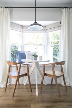 two chairs and a table in front of a window with white drapes on the windowsill