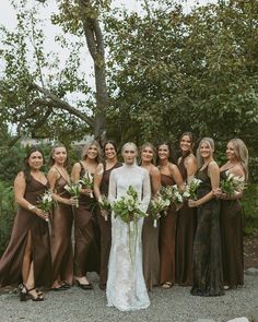 a group of women standing next to each other in front of a tree and bushes