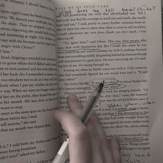 a hand holding a pen over an open book with writing on the pages in cursive handwriting