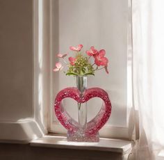 a heart shaped vase with flowers in it sitting on a window sill next to a curtain