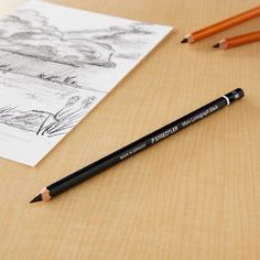 two pencils sitting on top of a wooden table next to a drawing and pen