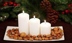 four white candles sitting on top of a plate filled with nuts next to a christmas tree