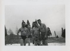 three men in bathing suits standing next to each other with trees in the back ground