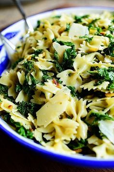 a bowl filled with pasta and spinach on top of a wooden table