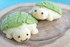 two cookies shaped like turtles with green leaves on them sitting on top of a wooden plate