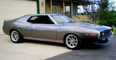 a gray muscle car parked in front of a house with two garage doors on the side