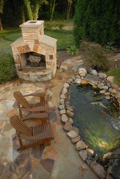 an outdoor fireplace with chairs around it and a fish pond in the backround