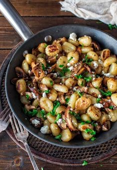 a skillet filled with potatoes and onions on top of a wooden table next to a fork