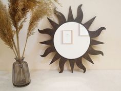 a mirror and vase with dried plants in it on a table next to a wall