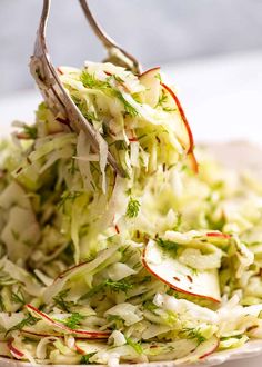 a plate with shredded cabbage and radishes on it is being held by tongs