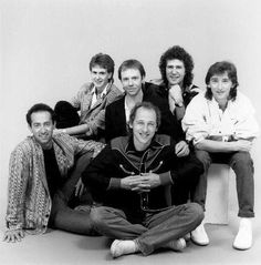 a group of men sitting next to each other in front of a white wall with one man smiling at the camera