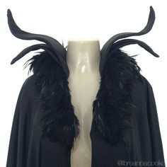 a white mannequin wearing a black cape with feathers on it's shoulders