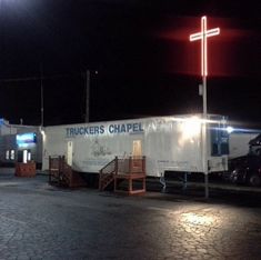 a white truck parked in front of a gas station at night with a cross on it's side