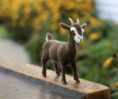 a small toy goat standing on top of a wooden table next to flowers and bushes