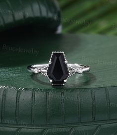 a black diamond ring sitting on top of a green tire treaded surface with leaves in the background