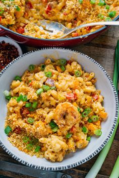 two bowls filled with macaroni and cheese on top of a wooden table next to green onions