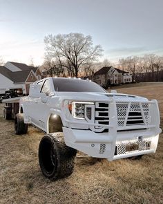 a large white truck parked on top of a grass covered field next to a house