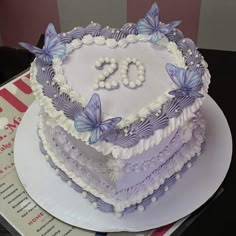 a heart shaped cake decorated with butterflies on top of a table next to a magazine