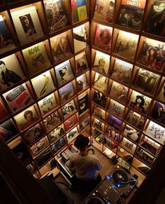 a man sitting at a desk in front of a wall full of records and cds