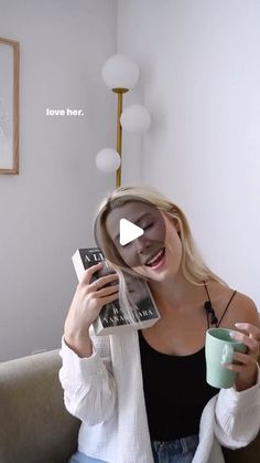 a woman sitting on top of a couch holding a coffee cup and reading a book