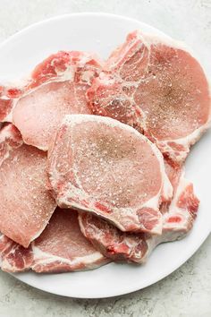 raw pork chops on a white plate with seasoning sprinkled over them