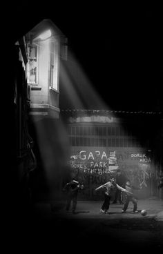 some people playing soccer in the dark on a street at night with light coming through