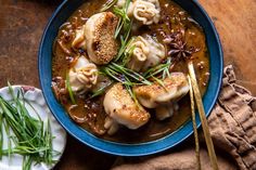 a blue bowl filled with dumplings covered in sauce and garnished with green onions