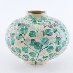 a blue and white vase with leaves painted on the front, sitting against a white background