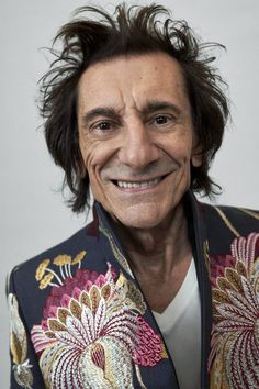 a man with long hair and a smile on his face, wearing a colorful jacket