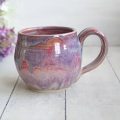 a coffee cup sitting on top of a wooden table next to a purple and white flower