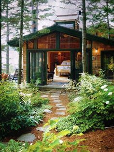 a small cabin in the woods surrounded by greenery and trees with a bed on it