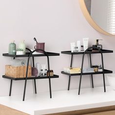 two black shelves with various items on them in front of a white wall and mirror