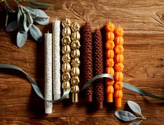 an assortment of decorative candles are arranged on a wooden table with eucalyptus leaves and ribbons