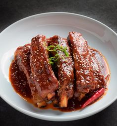 two pieces of meat covered in sauce on a white plate