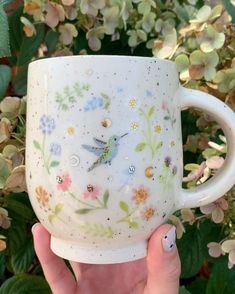 a hand holding a coffee cup with flowers painted on the side and a bird sitting on it