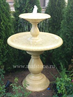 a bird is sitting on top of a fountain in the middle of some bushes and trees