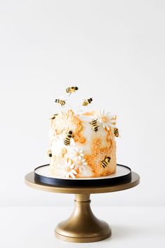 a cake with white frosting and yellow flowers on a gold plate, topped with bees