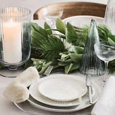 the table is set with white plates, silverware and greenery as well as candles