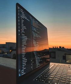 an open laptop computer sitting on top of a wooden table in front of a sunset