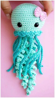 a crocheted octopus with a pink bow on its head is being held by someone's hand