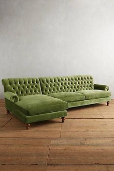 a green couch sitting on top of a hard wood floor next to a white wall