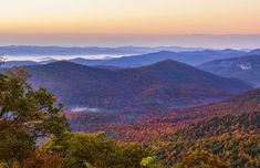 the mountains are covered in colorful foliage and fog at sunrise or sunset as seen from high above