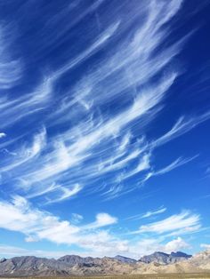 there are many clouds in the sky above some mountains and grass on the ground below