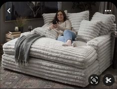 a woman is sitting on a couch made out of blankets and pillows while looking at her cell phone